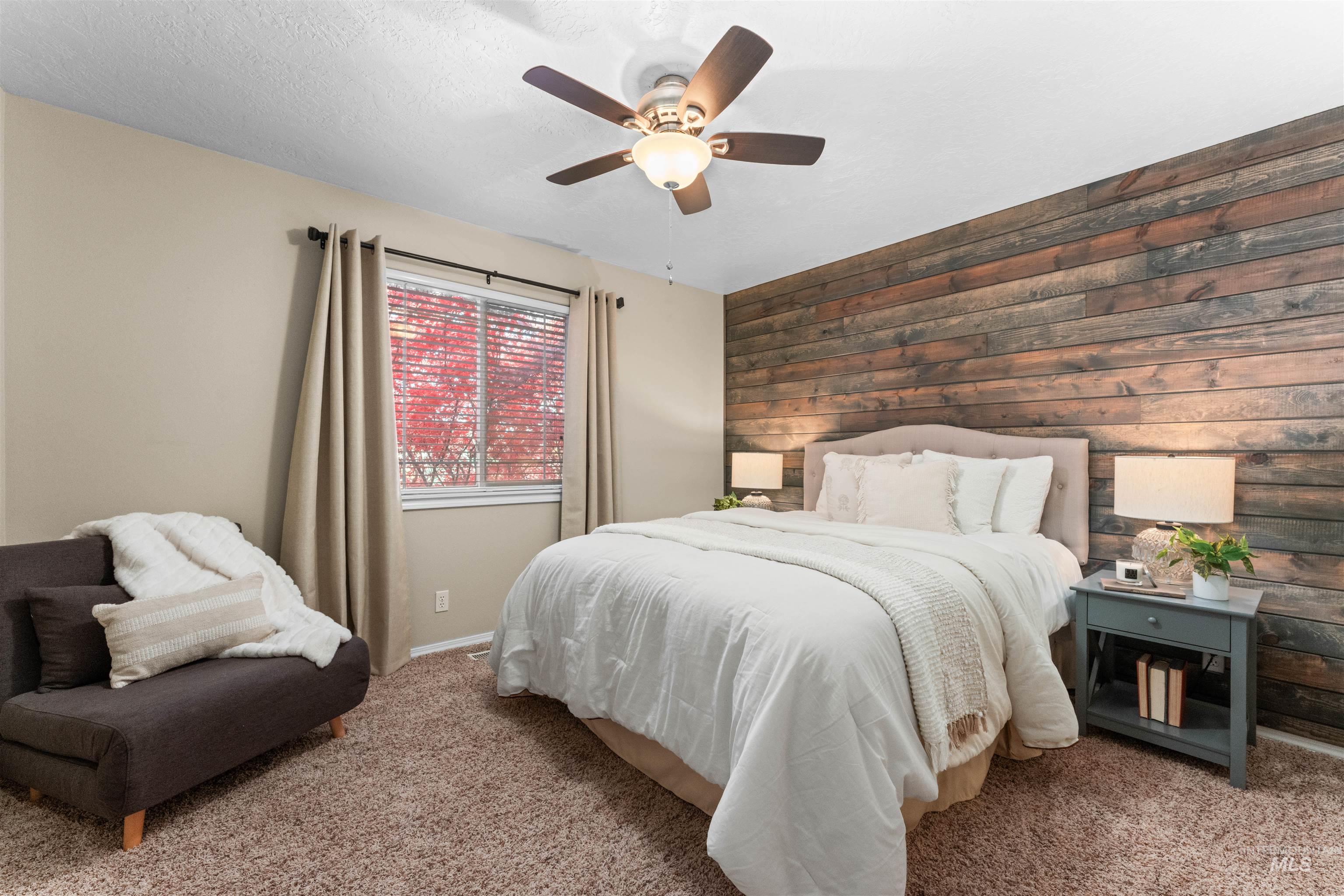 Carpeted bedroom featuring wood walls, an accent wall, a ceiling fan, and a textured ceiling