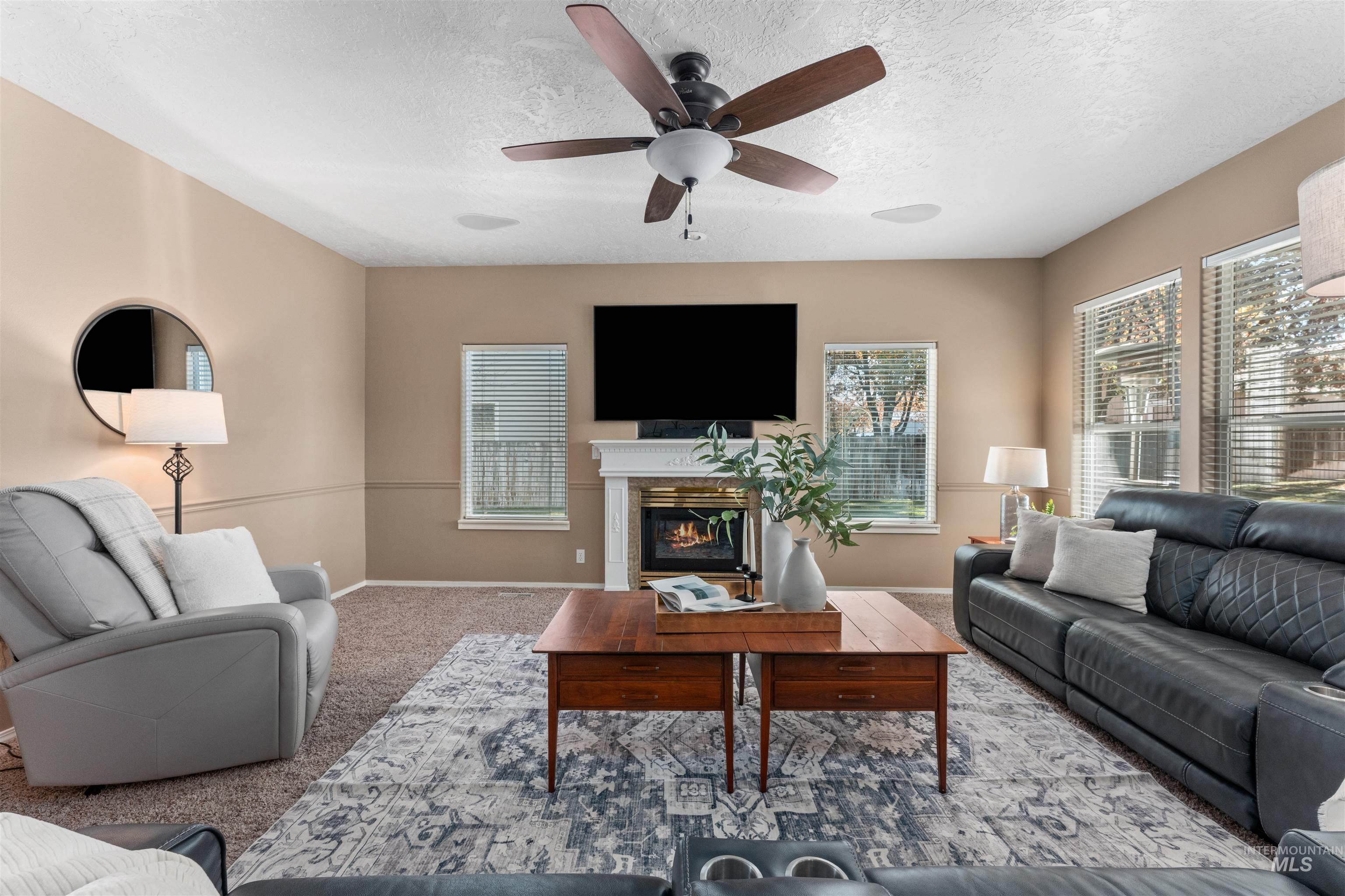 Carpeted living area featuring a textured ceiling, a glass covered fireplace, and ceiling fan