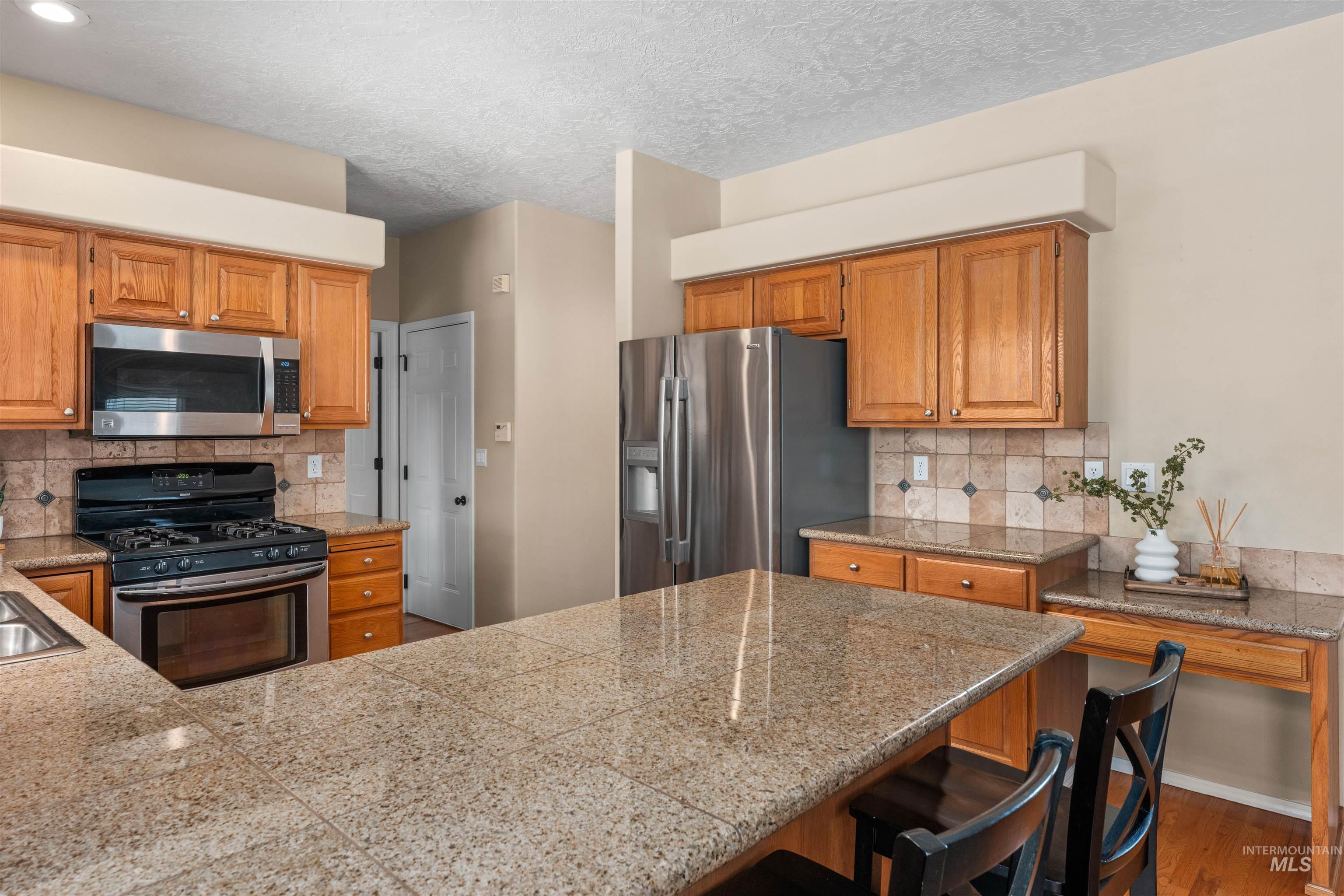 Kitchen with appliances with stainless steel finishes, backsplash, tile counters, dark wood-style floors, and a textured ceiling