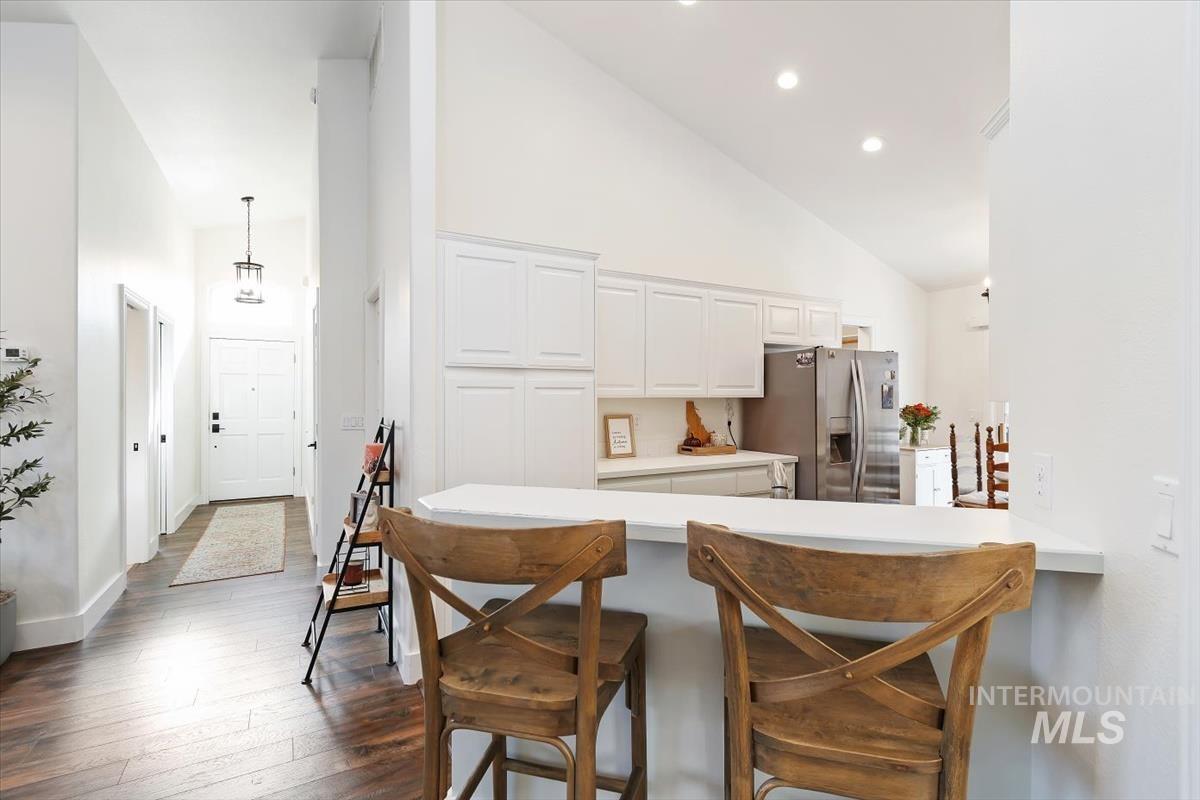 Kitchen featuring a breakfast bar, high vaulted ceiling, a peninsula, light countertops, and stainless steel refrigerator with ice dispenser