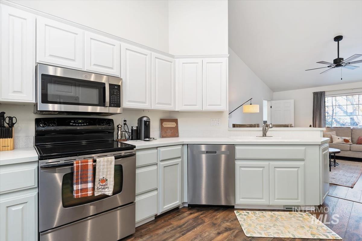 Kitchen featuring stainless steel appliances, white cabinetry, dark wood-type flooring, lofted ceiling, and open floor plan