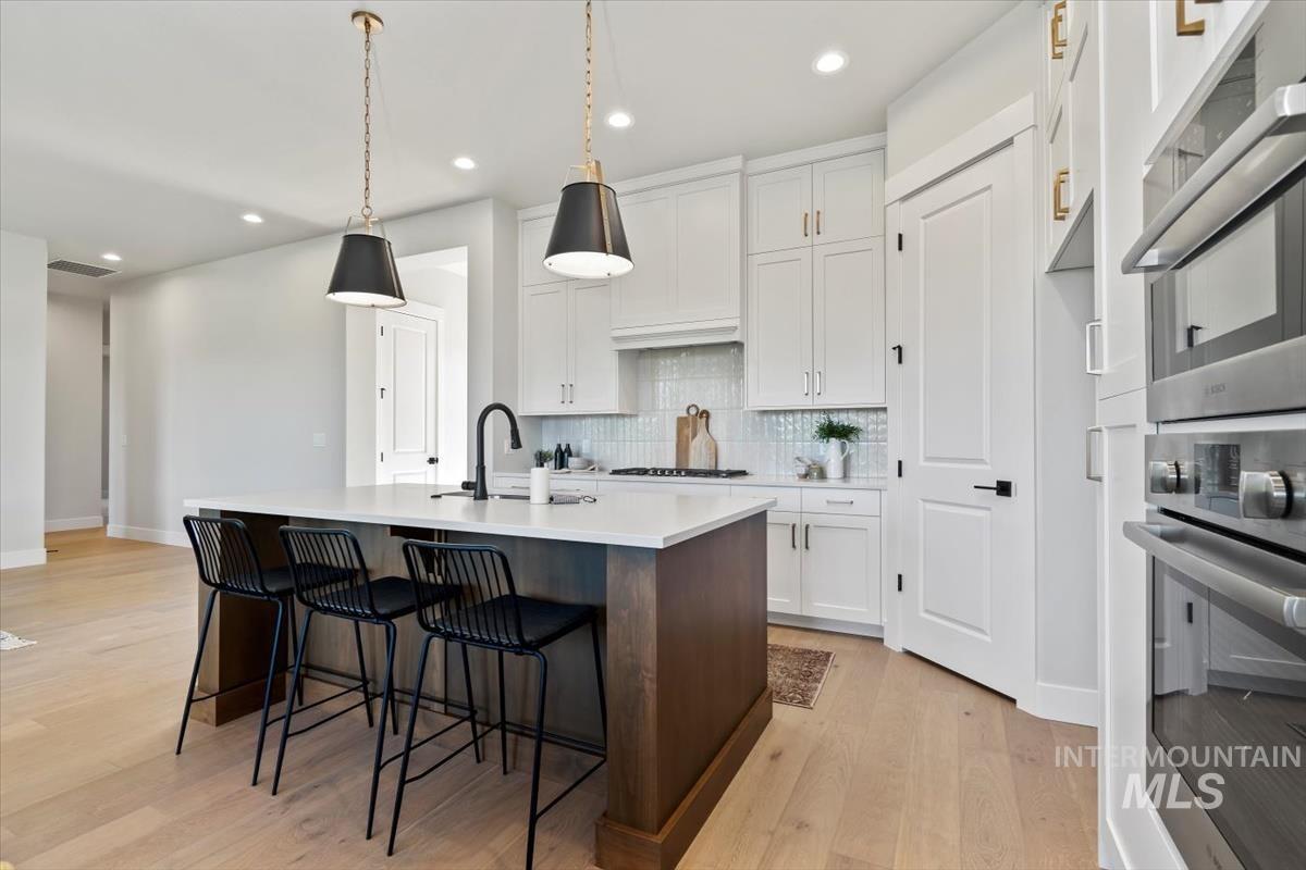 Kitchen featuring double oven, a kitchen island with sink, white cabinets, pendant lighting, and recessed lighting