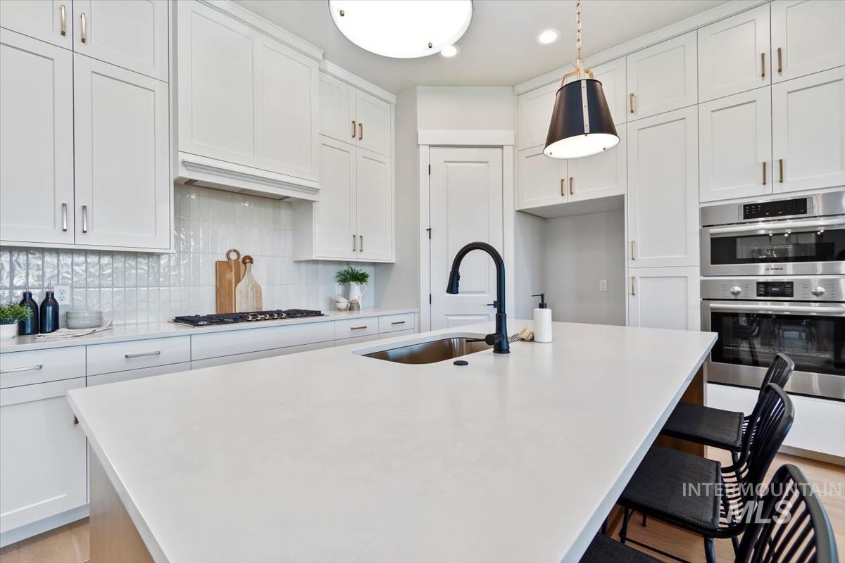 Kitchen featuring white cabinets, a kitchen breakfast bar, tasteful backsplash, stainless steel double oven, and recessed lighting