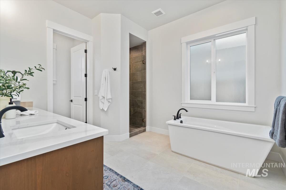 Bathroom featuring a freestanding bath, double vanity, a shower stall, and light tile patterned floors