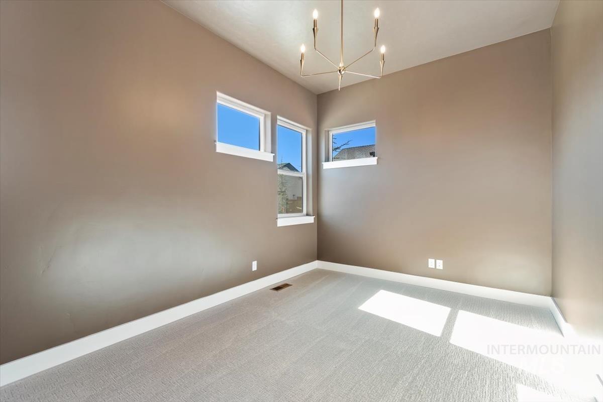 Carpeted spare room featuring baseboards and a chandelier