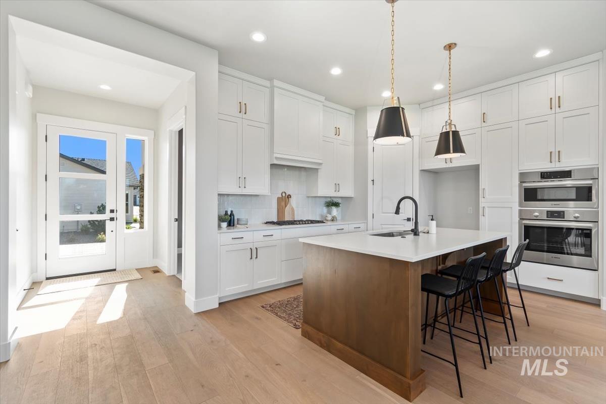 Kitchen with white cabinetry, light wood-style floors, an island with sink, tasteful backsplash, and brown cabinets