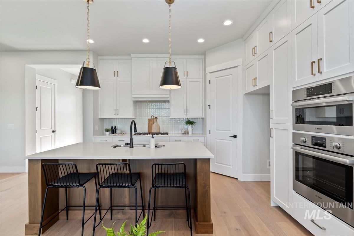 Kitchen with double oven, white cabinets, a breakfast bar area, pendant lighting, and light wood-style flooring