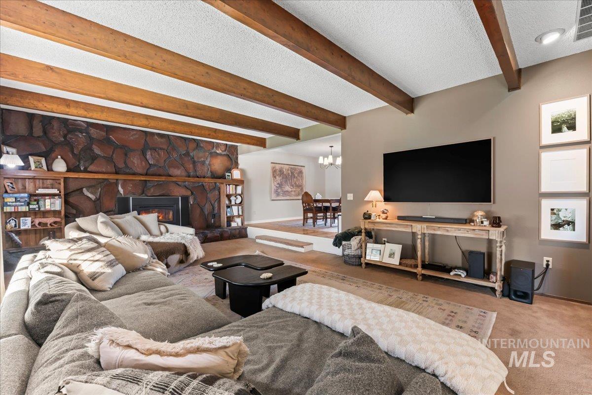 Carpeted living room with beam ceiling, a textured ceiling, a fireplace, and a chandelier