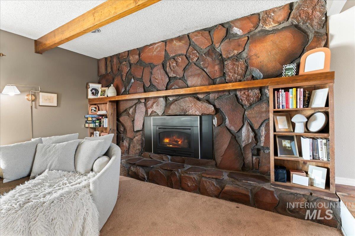 Living area featuring a fireplace, a textured ceiling, beamed ceiling, and carpet
