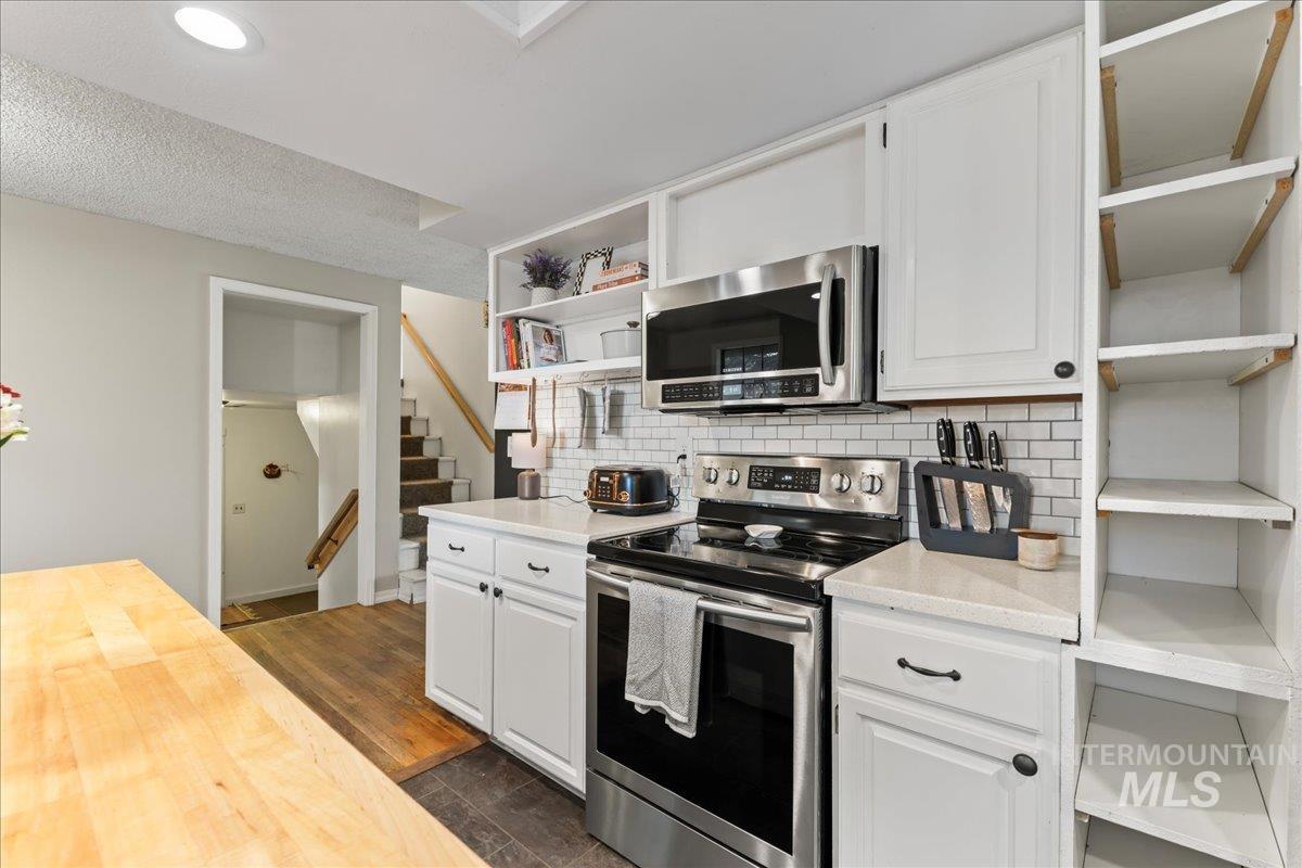 Kitchen featuring open shelves, appliances with stainless steel finishes, decorative backsplash, white cabinetry, and wooden counters