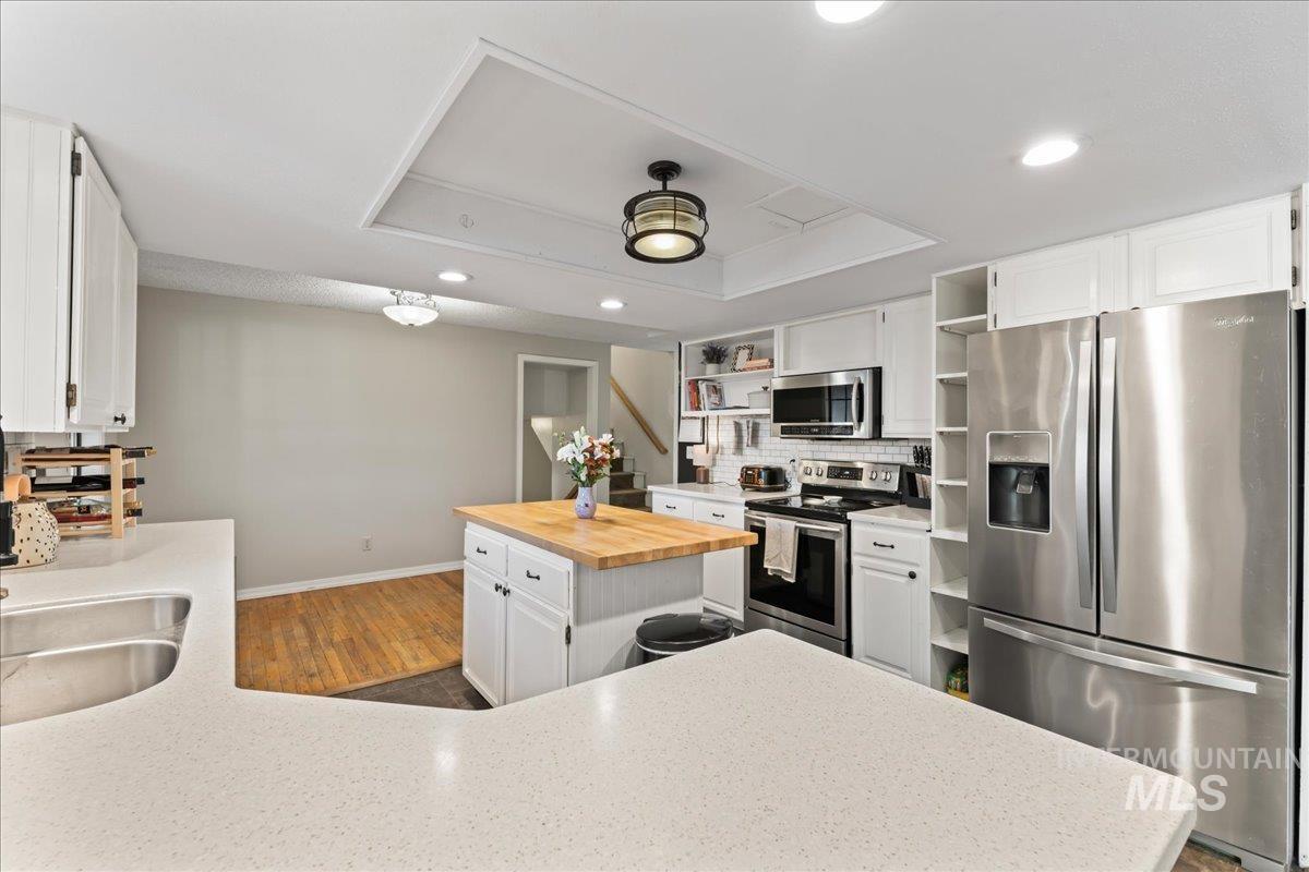 Kitchen featuring open shelves, stainless steel appliances, white cabinets, a tray ceiling, and wood counters