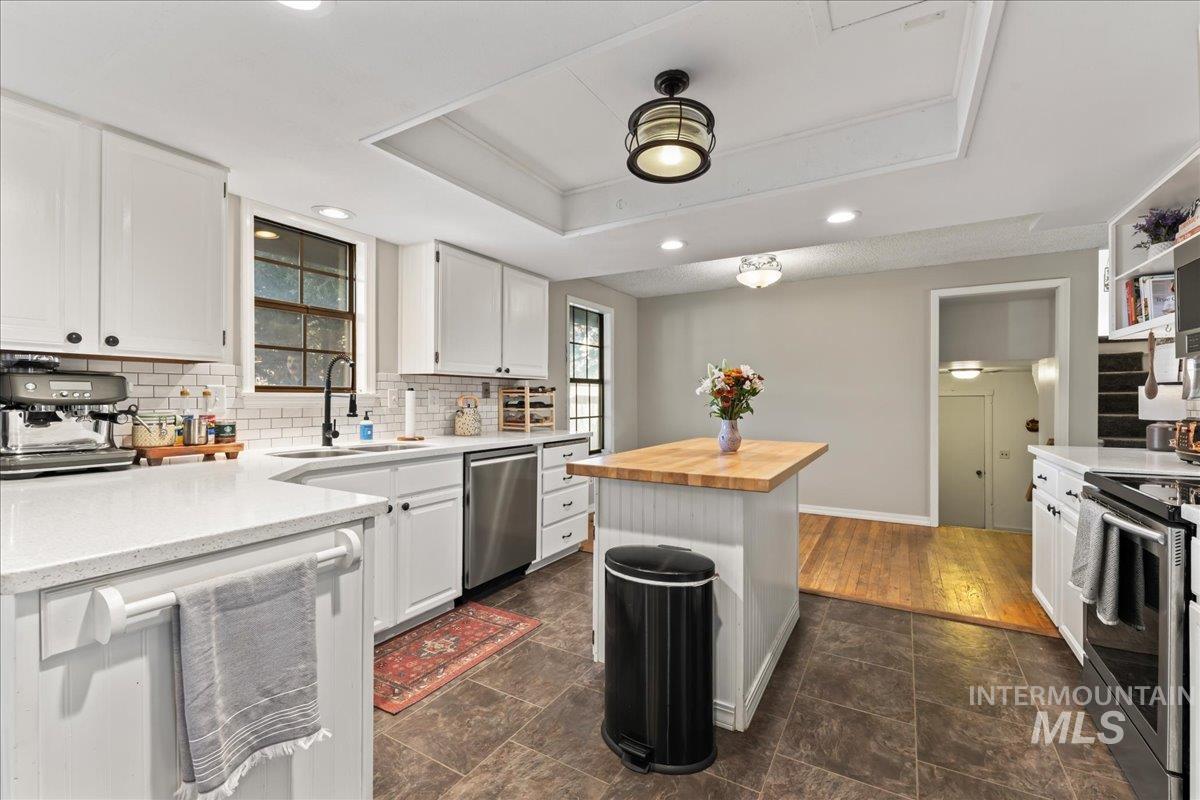 Kitchen featuring white cabinets, wood counters, appliances with stainless steel finishes, a tray ceiling, and tasteful backsplash