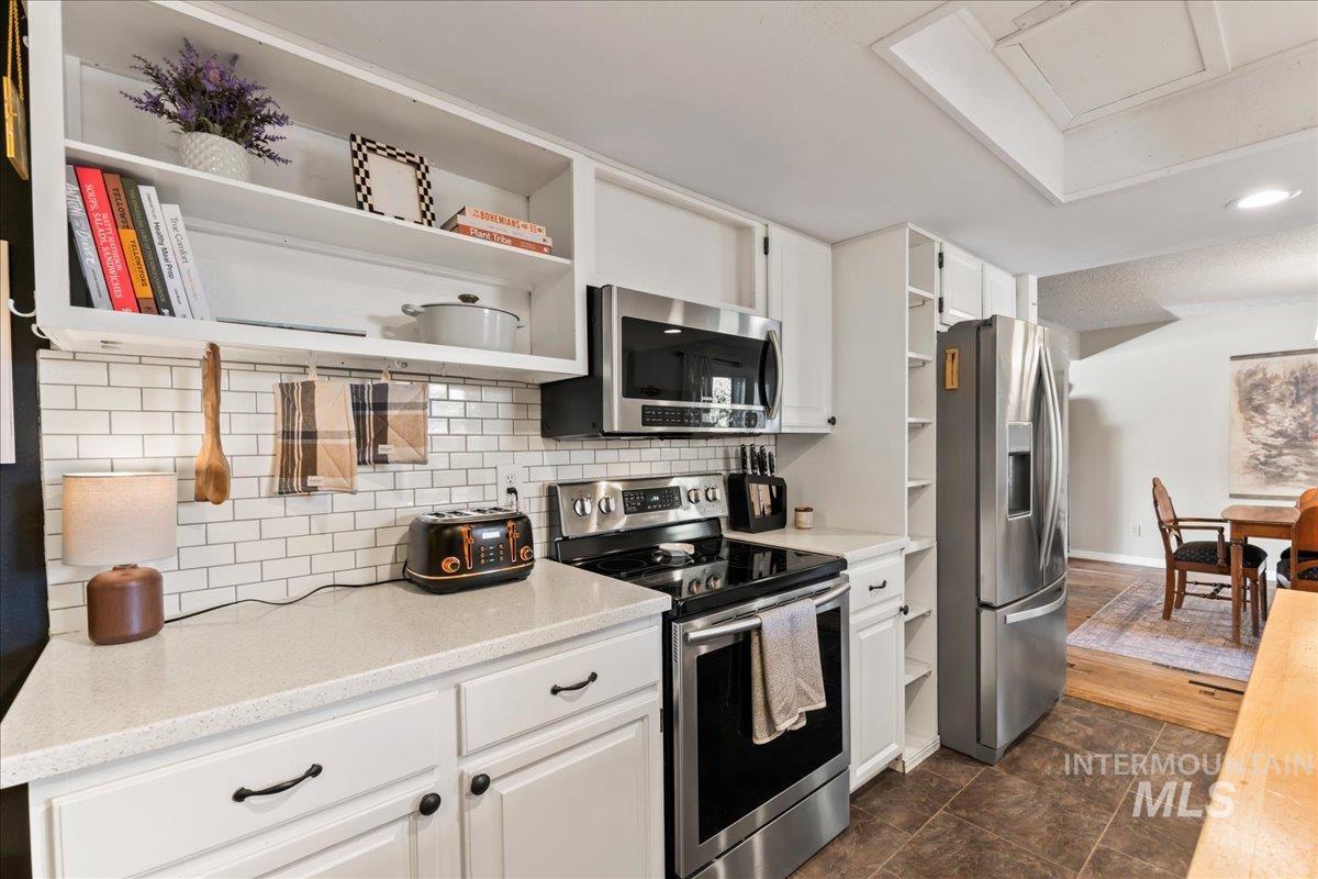 Kitchen with open shelves, stainless steel appliances, white cabinets, tasteful backsplash, and recessed lighting