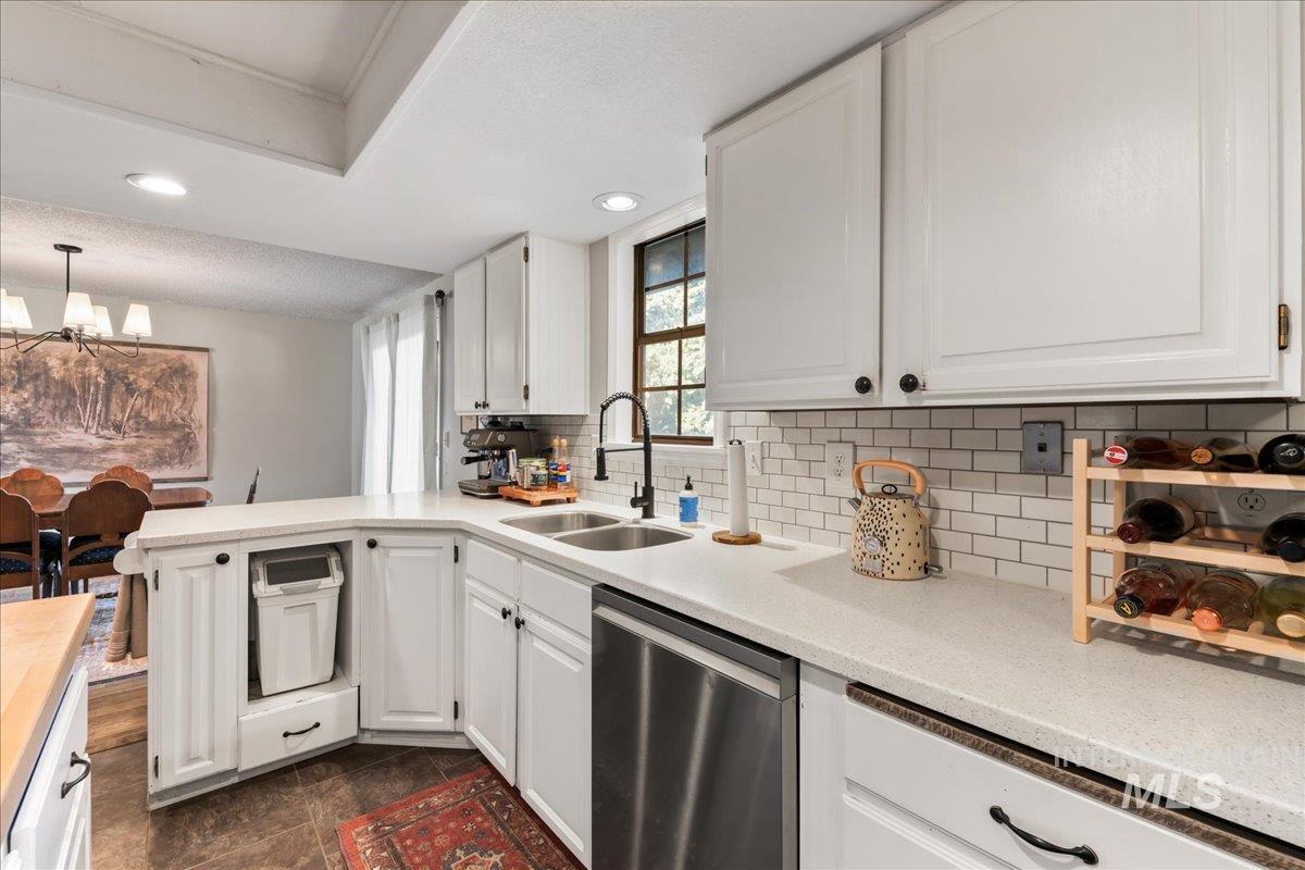 Kitchen with tasteful backsplash, dishwasher, white cabinetry, a chandelier, and a peninsula