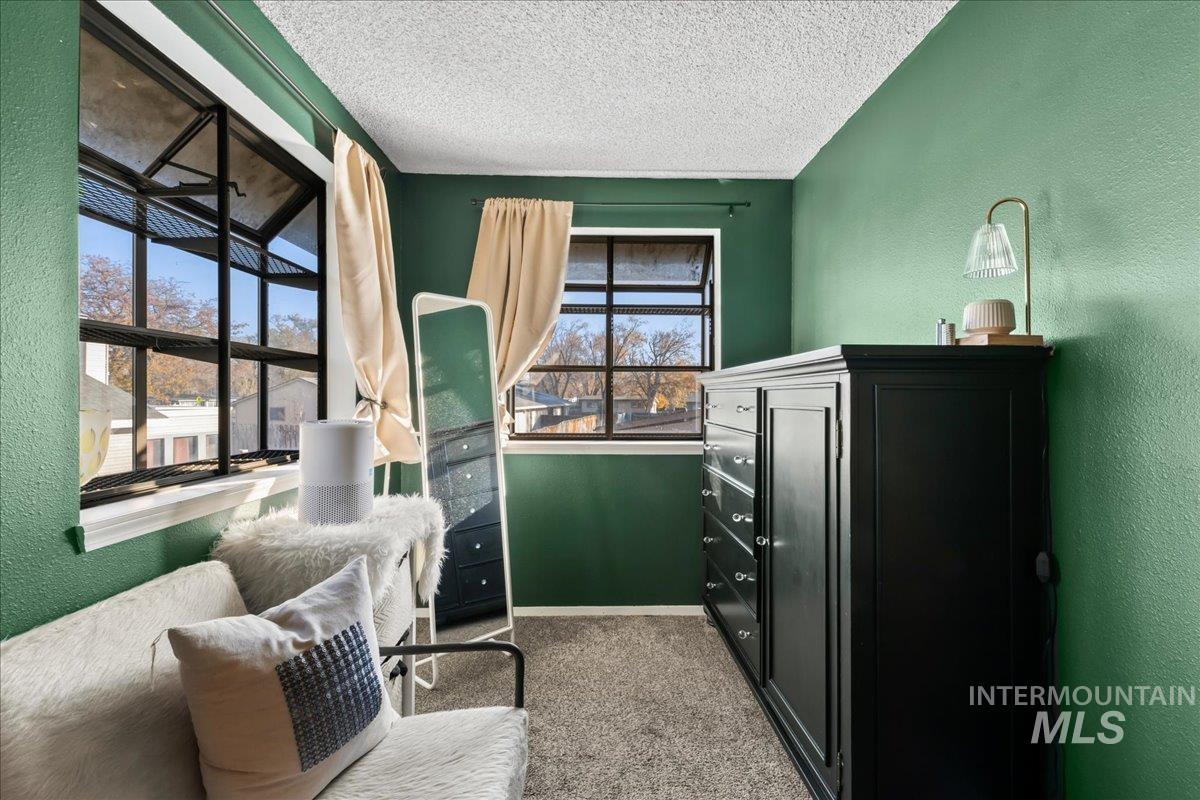 Living area featuring a textured wall, light carpet, and a textured ceiling