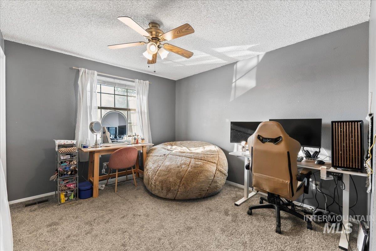 Carpeted bedroom with a desk, ceiling fan, and a textured ceiling