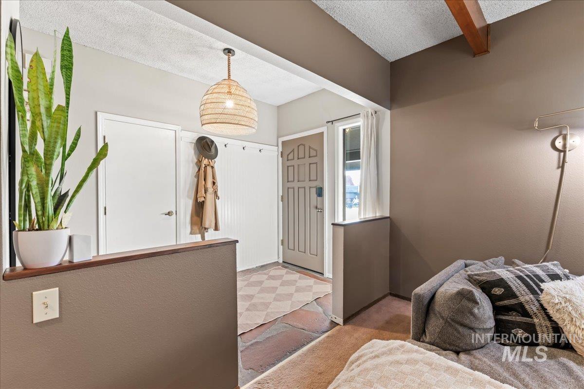 Foyer entrance featuring a textured ceiling, light carpet, light floors, and beam ceiling