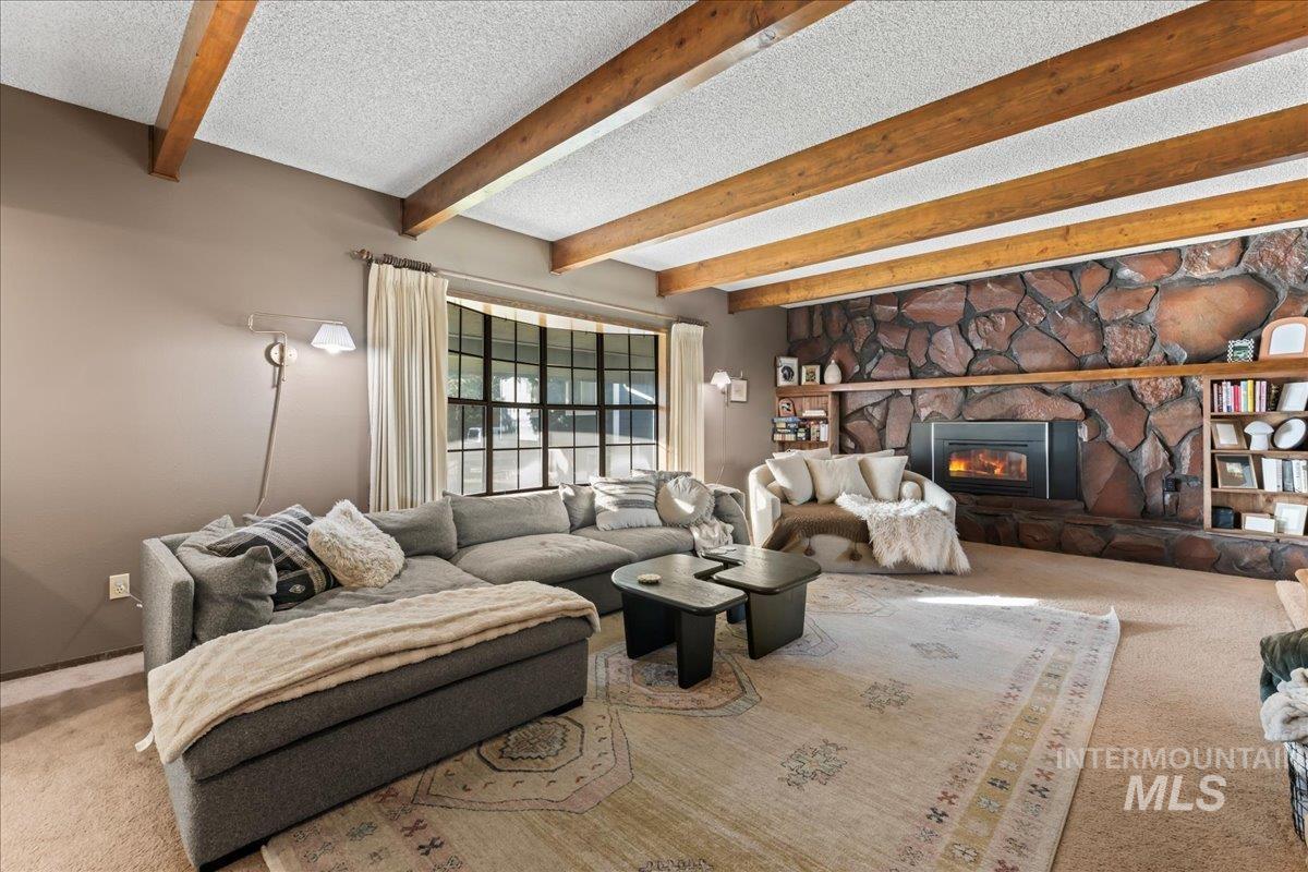 Living room with carpet, beamed ceiling, a textured ceiling, and a fireplace