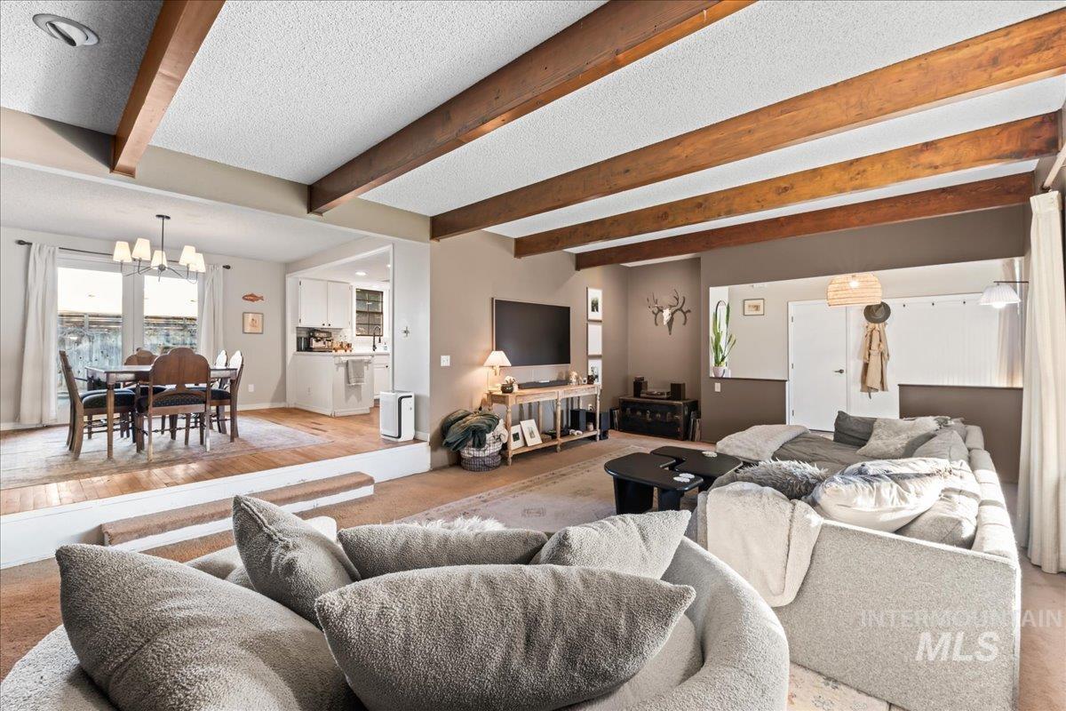 Living area featuring beam ceiling, a textured ceiling, a chandelier, and wood finished floors