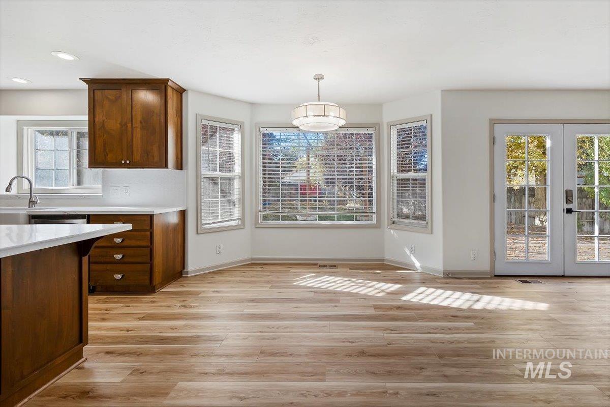 Kitchen featuring french doors, light wood-style flooring, hanging light fixtures, and brown cabinetry