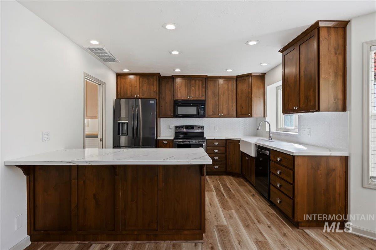 Kitchen with a peninsula, black appliances, light wood-style flooring, decorative backsplash, and light stone counters