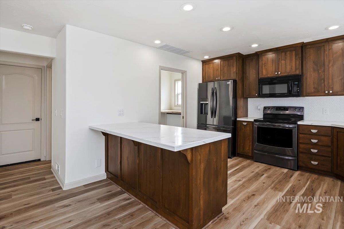 Kitchen featuring black appliances, dark brown cabinetry, a breakfast bar, a peninsula, and light wood finished floors