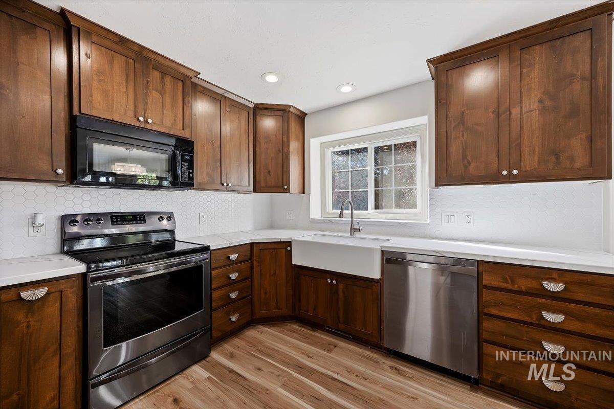 Kitchen with stainless steel appliances, light wood-style floors, backsplash, dark brown cabinets, and recessed lighting