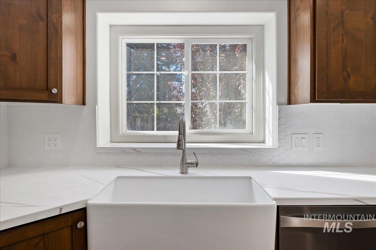Kitchen view of tasteful backsplash, stainless steel dishwasher, dark brown cabinetry, and light stone counters
