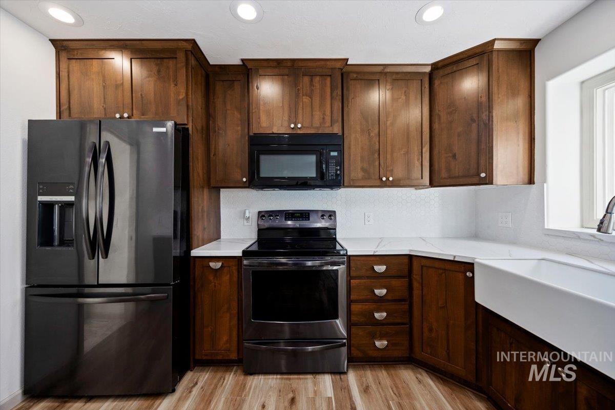Kitchen with black appliances, light wood-style flooring, light stone counters, recessed lighting, and dark brown cabinetry