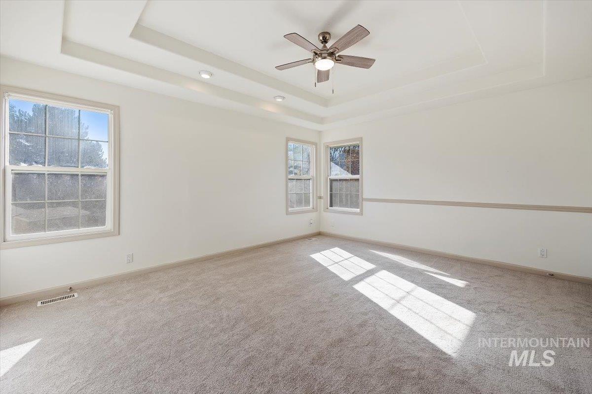 Empty room featuring a tray ceiling, carpet, and a ceiling fan