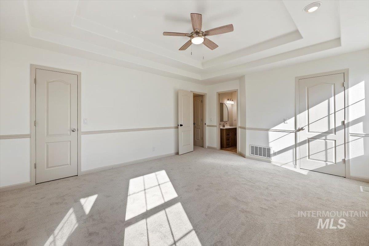 Unfurnished bedroom featuring a raised ceiling, carpet flooring, ensuite bath, and a ceiling fan