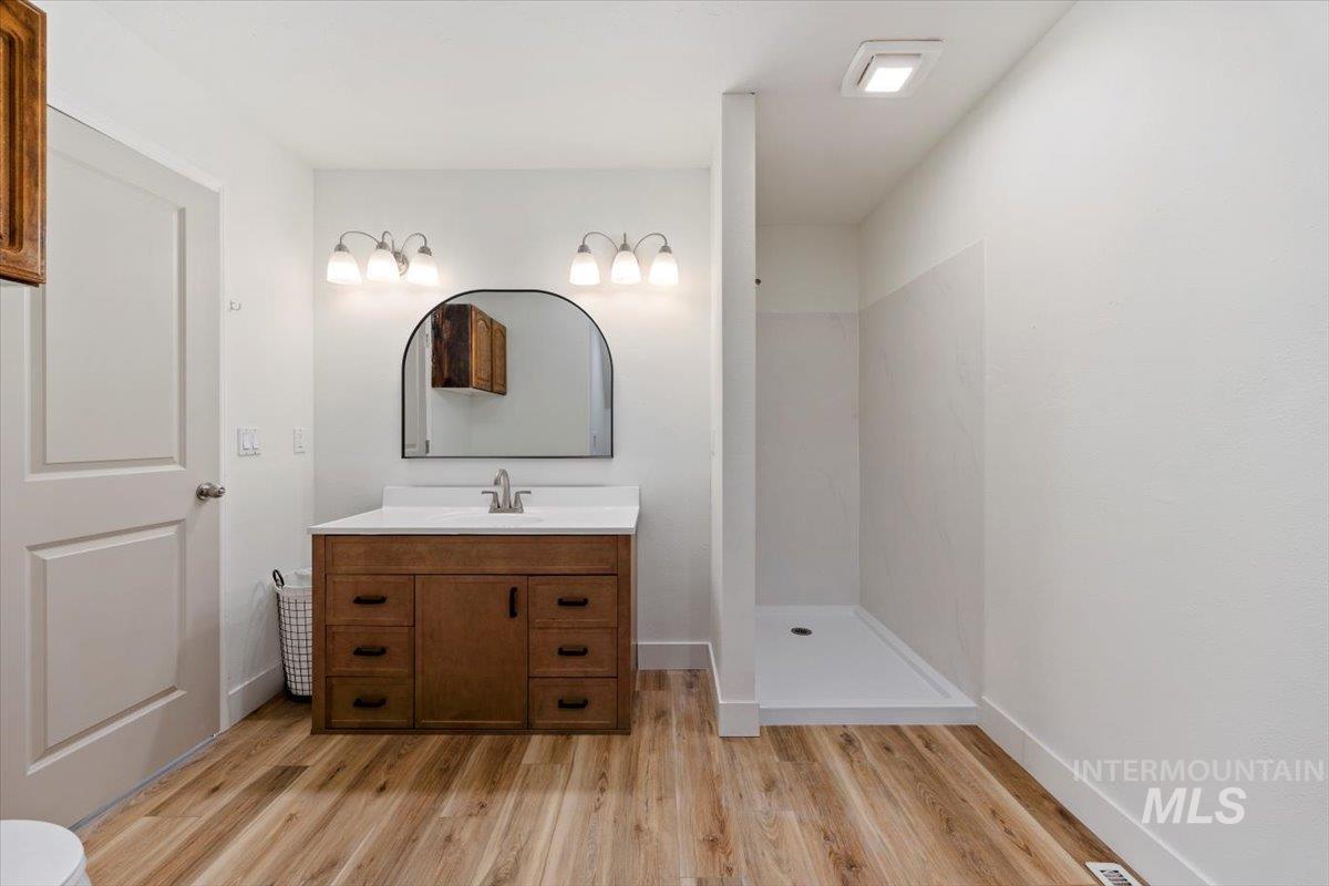 Full bathroom featuring light wood-style floors, a stall shower, and vanity