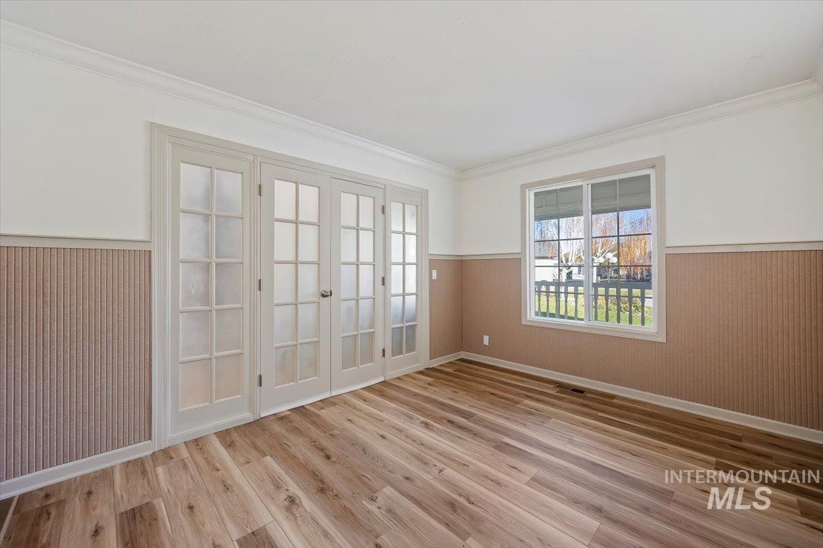 Spare room with a wainscoted wall, wood walls, crown molding, french doors, and light wood finished floors