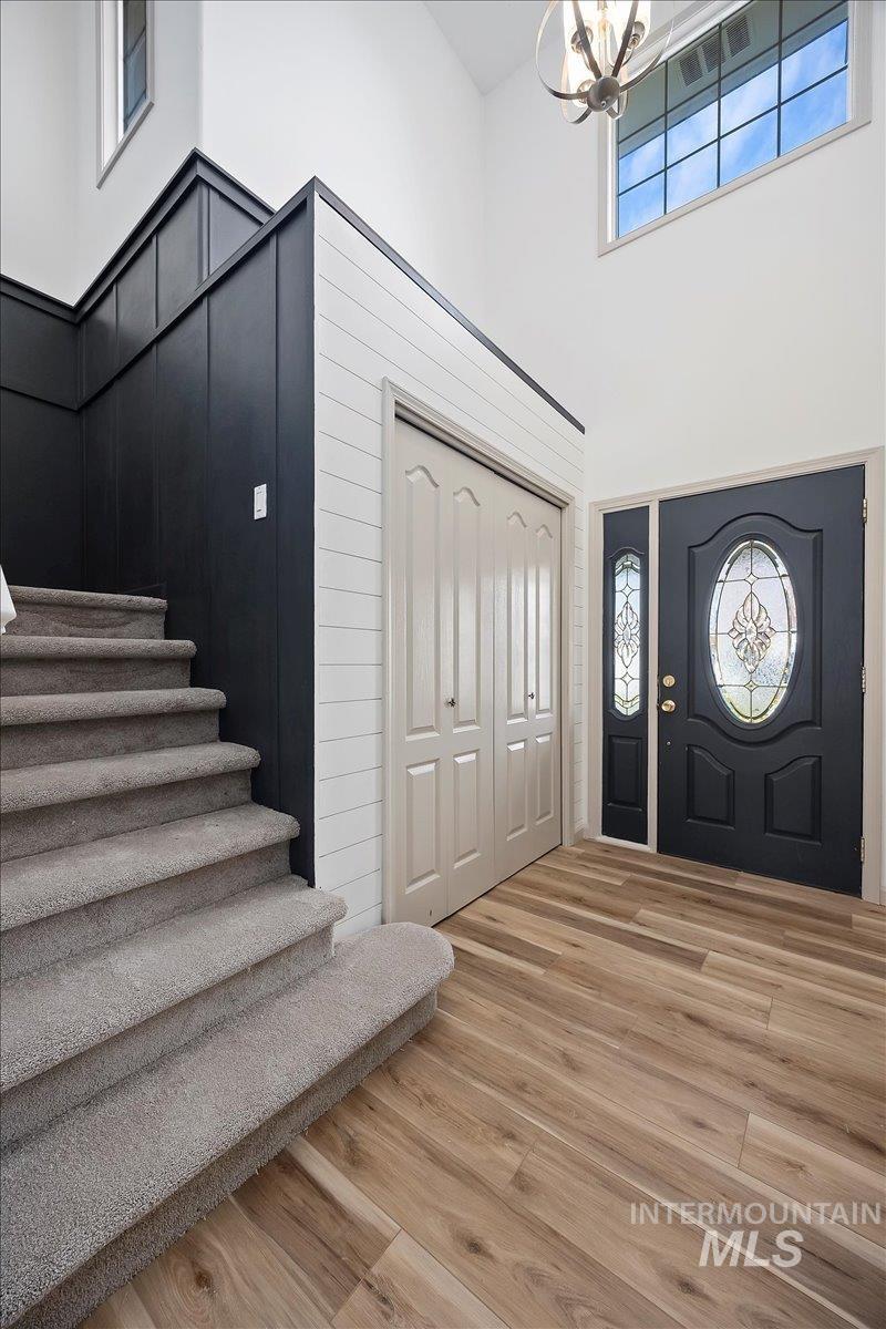 Entrance foyer with light wood-type flooring, a towering ceiling, stairs, and a chandelier