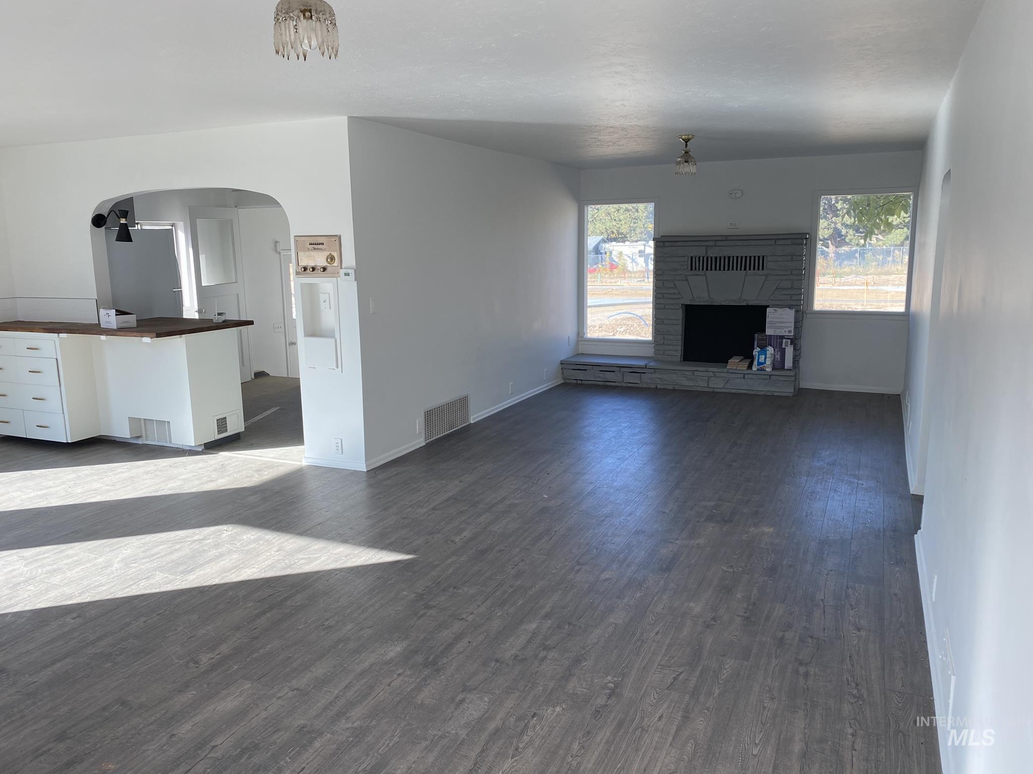 Unfurnished living room with dark wood finished floors, arched walkways, and a stone fireplace