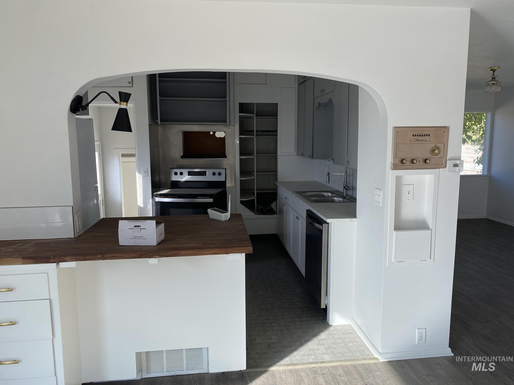 Kitchen featuring appliances with stainless steel finishes, white cabinets, arched walkways, and wood counters