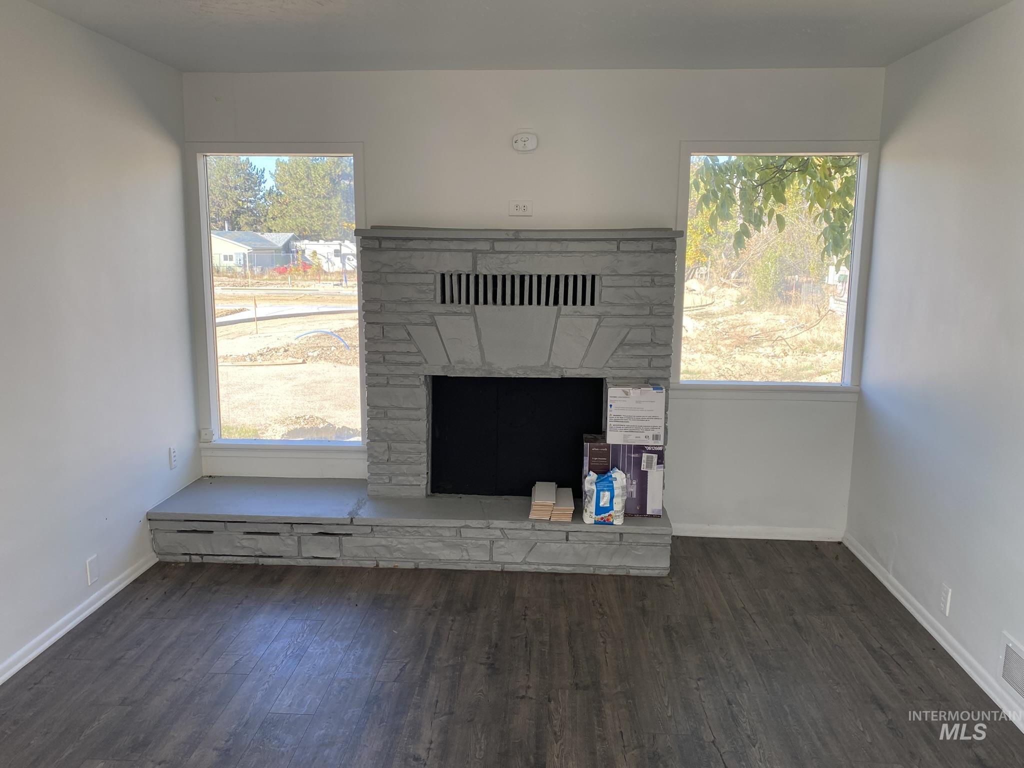 Unfurnished living room featuring dark wood finished floors and a fireplace with raised hearth