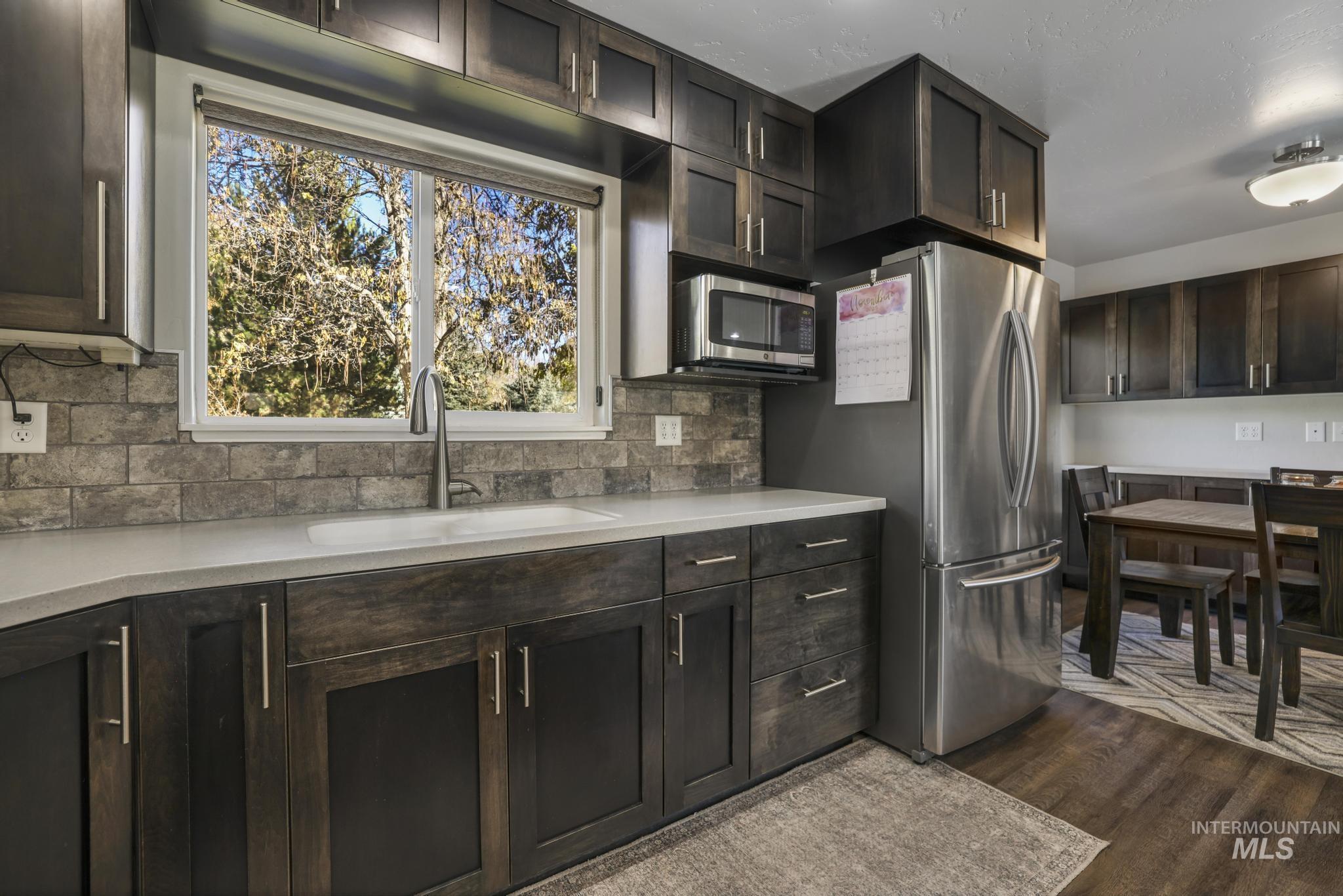 Kitchen with dark brown cabinetry, backsplash, stainless steel appliances, and dark wood-style floors