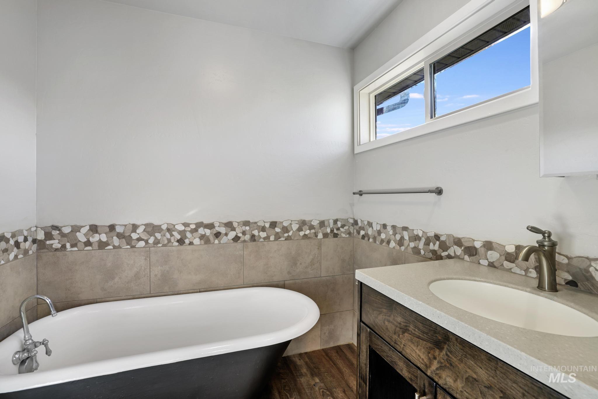 Bathroom featuring a freestanding tub, vanity, tile walls, wainscoting, and dark wood-type flooring