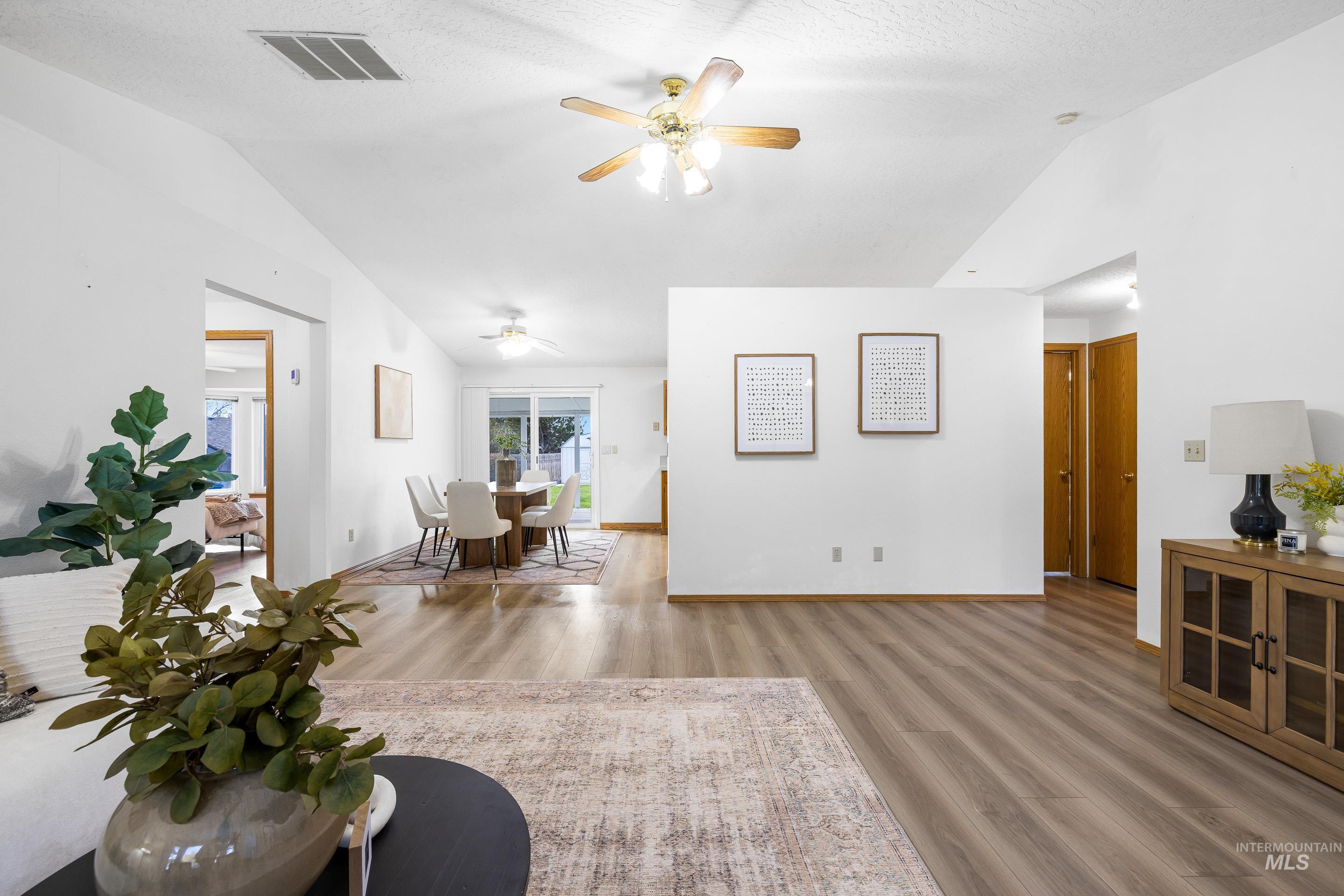 Living room with lofted ceiling, light wood-style flooring, ceiling fan, and a textured ceiling