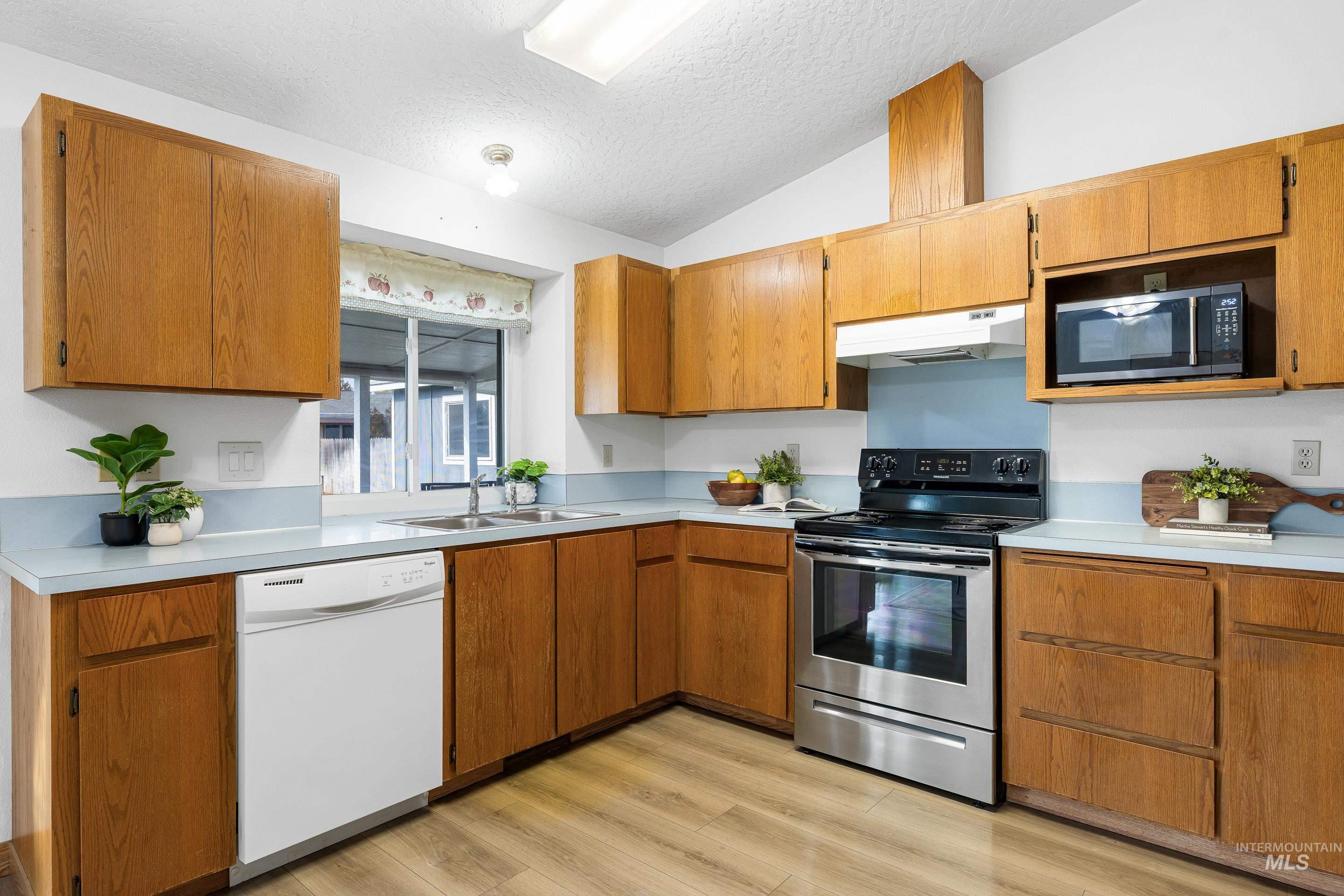 Kitchen featuring appliances with stainless steel finishes, a textured ceiling, light countertops, light wood-style flooring, and vaulted ceiling