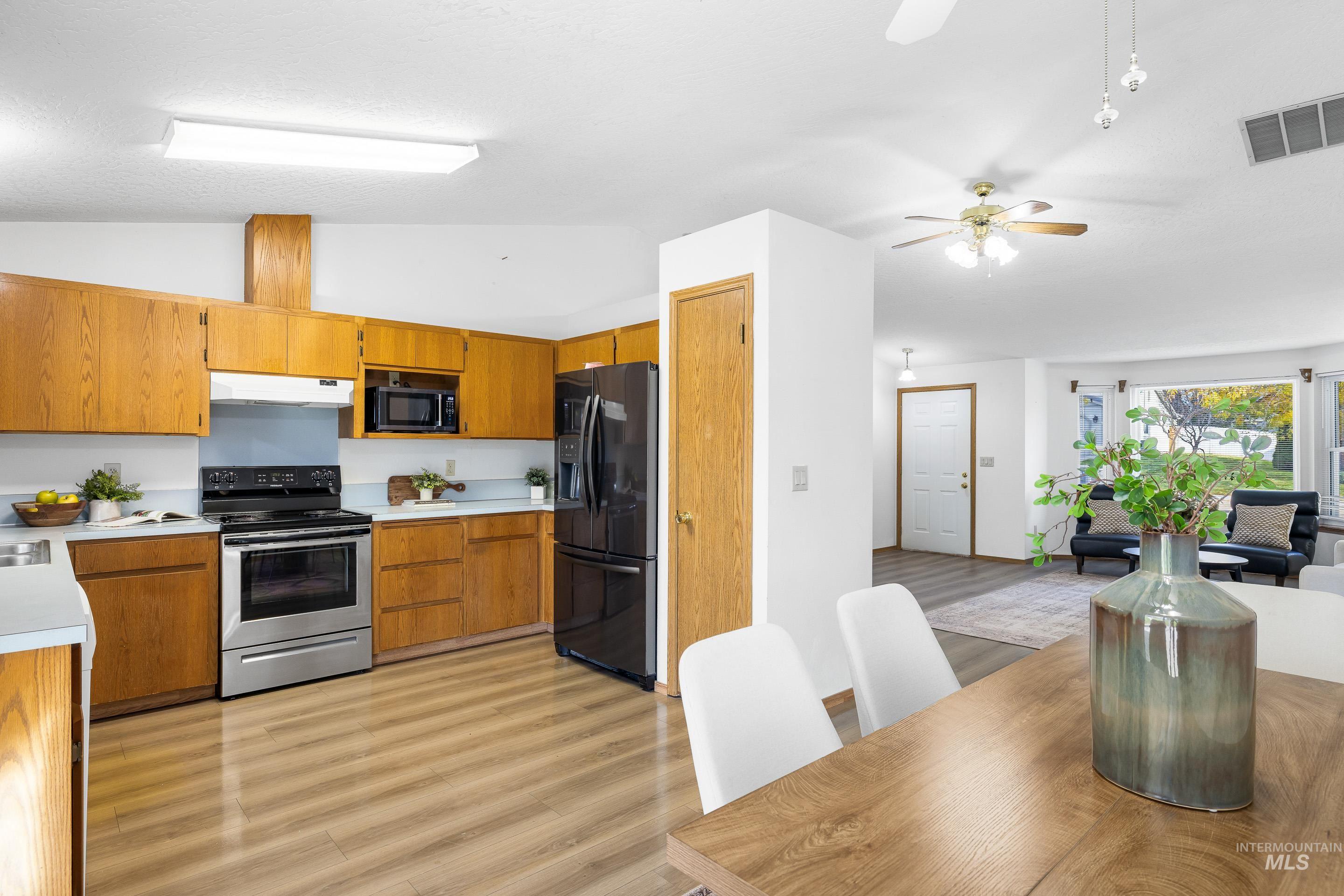 Kitchen featuring brown cabinetry, black appliances, light countertops, light wood finished floors, and vaulted ceiling
