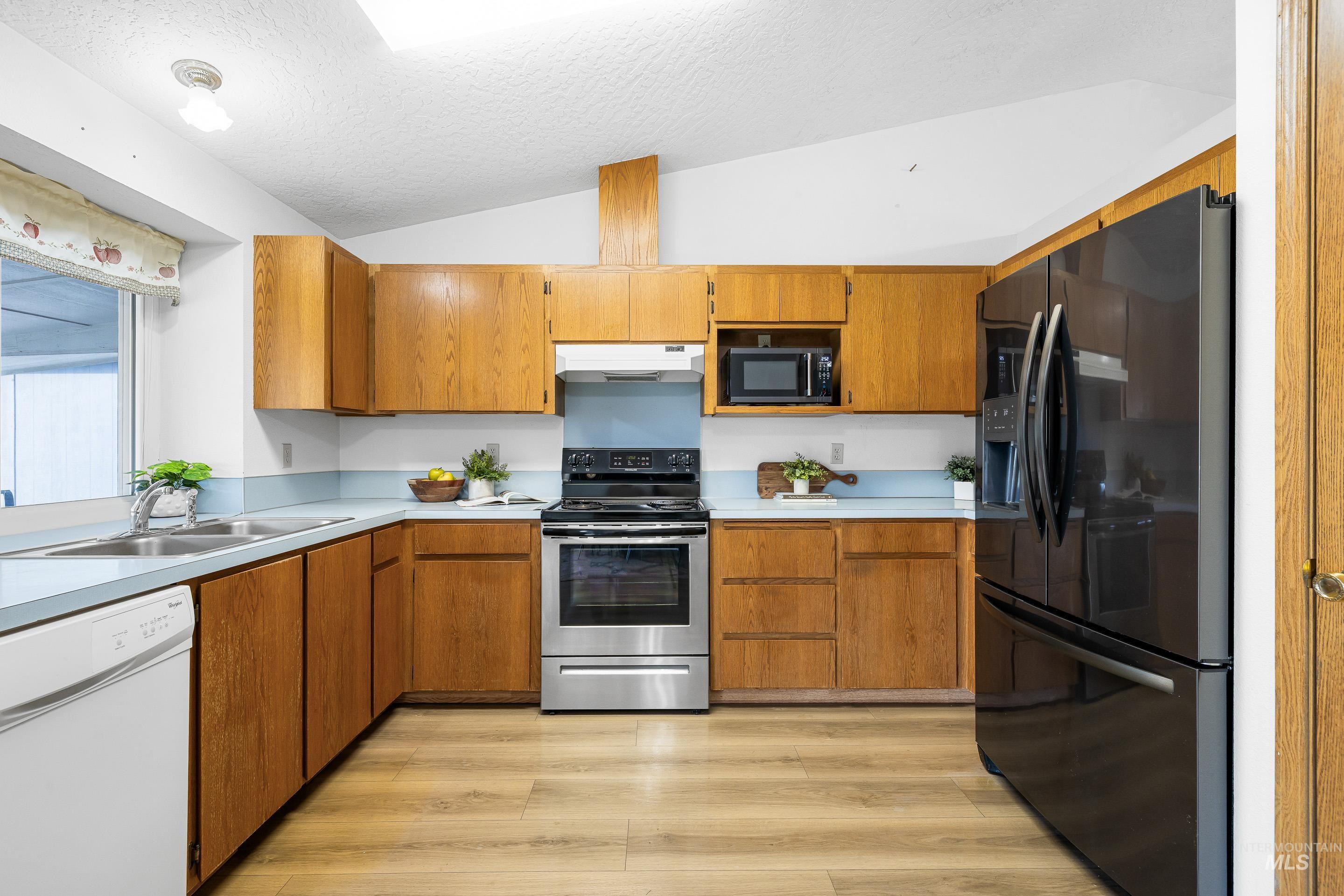 Kitchen featuring black appliances, brown cabinets, light countertops, a textured ceiling, and vaulted ceiling