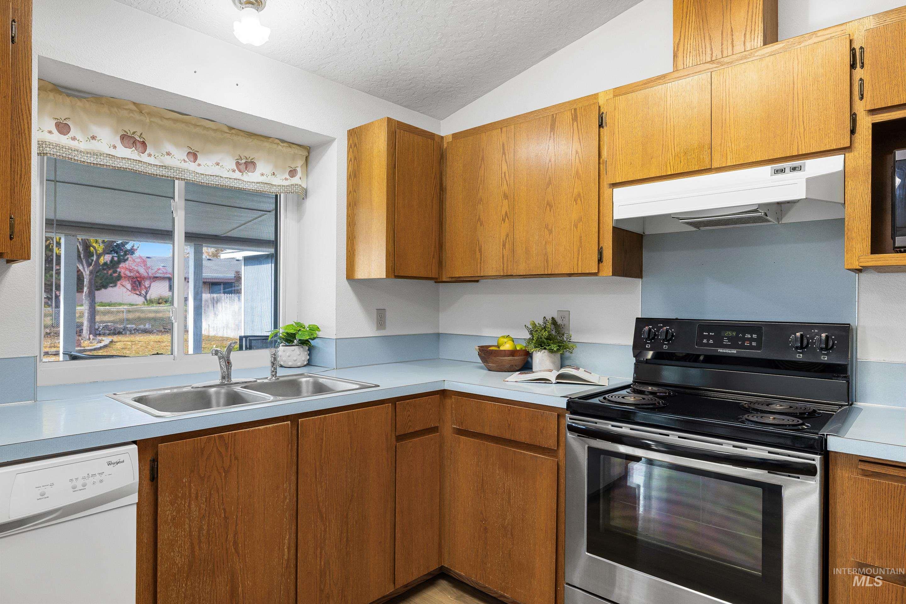 Kitchen with stainless steel range with electric cooktop, white dishwasher, a textured ceiling, brown cabinets, and under cabinet range hood