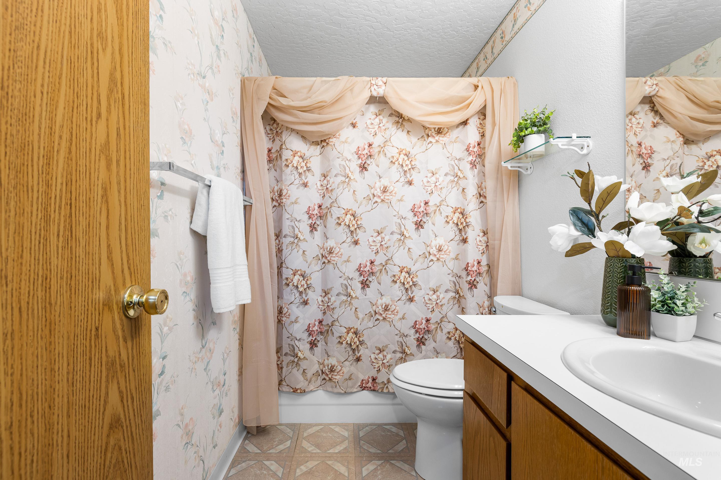 Bathroom with vanity, wallpapered walls, and a textured ceiling