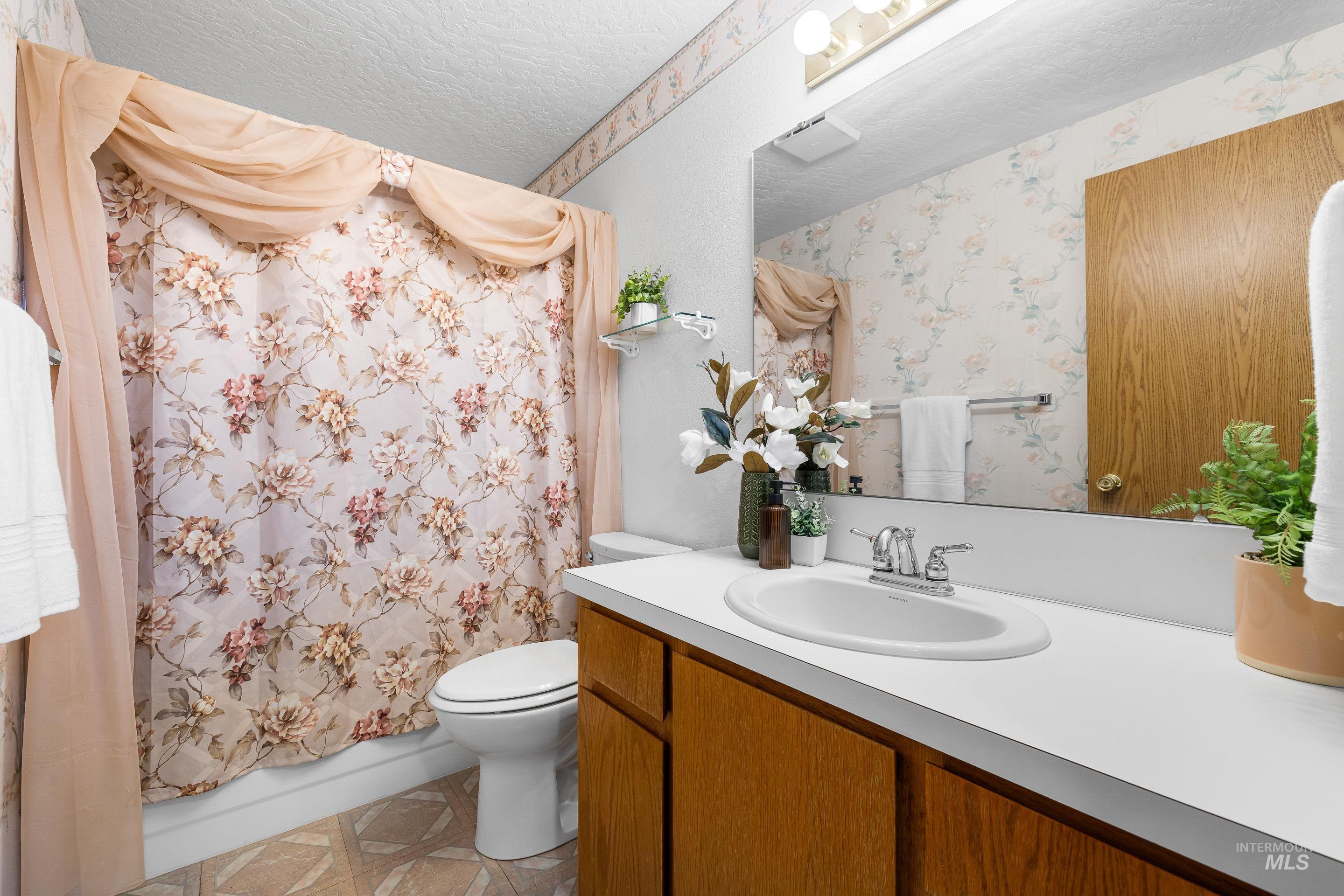 Bathroom featuring shower / tub combo with curtain, vanity, light tile patterned flooring, and a textured ceiling