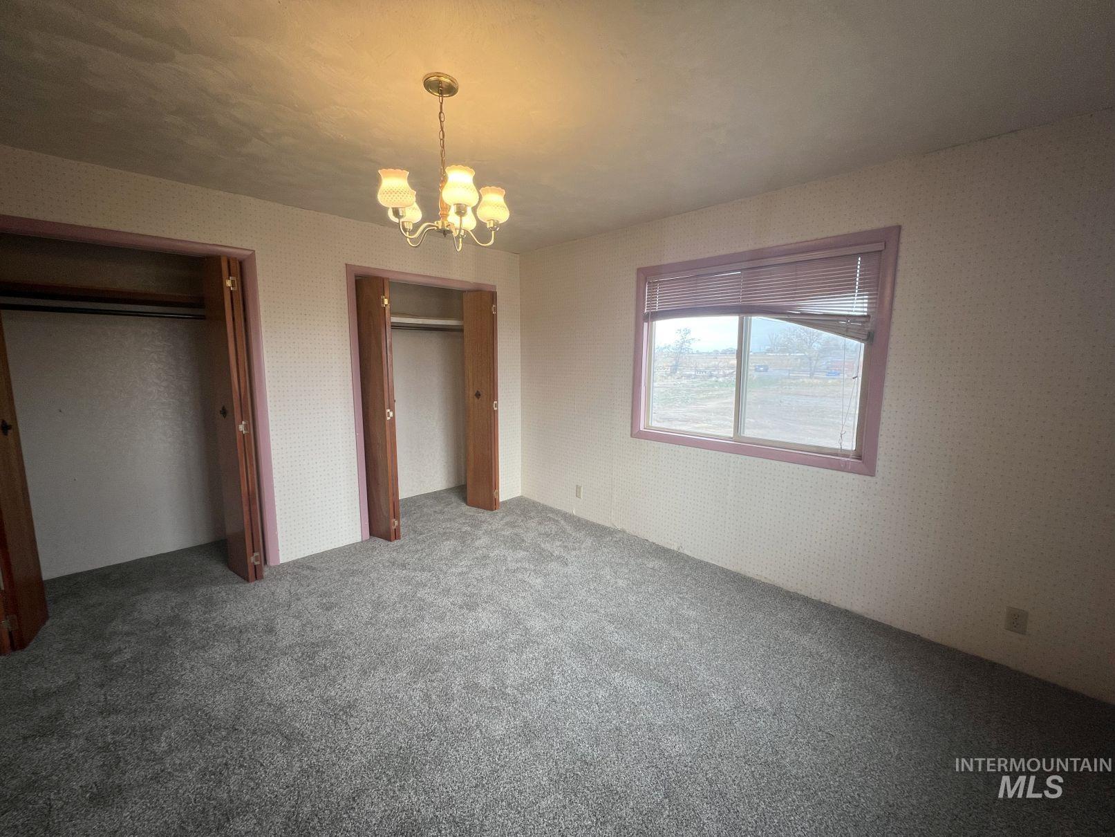 Unfurnished bedroom featuring a chandelier, two closets, and carpet flooring
