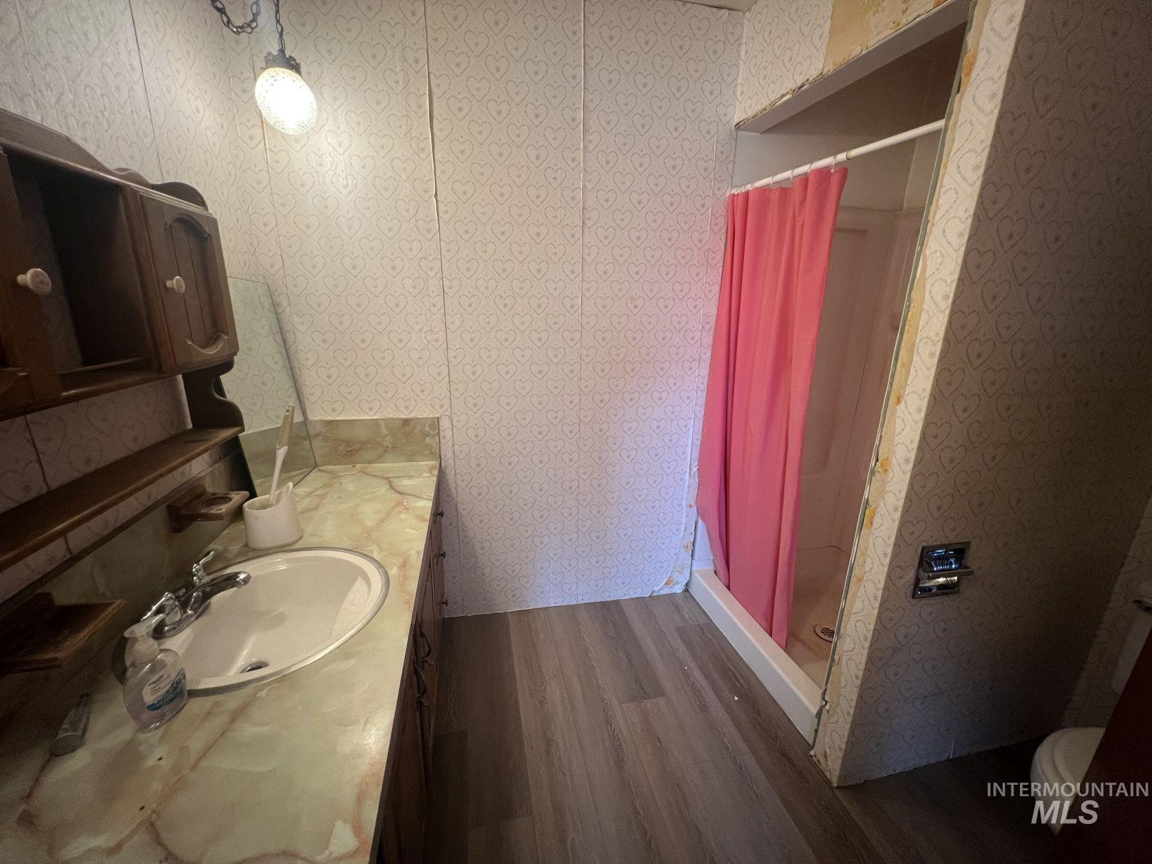 Full bathroom with a shower stall, dark wood-type flooring, vanity, and wallpapered walls