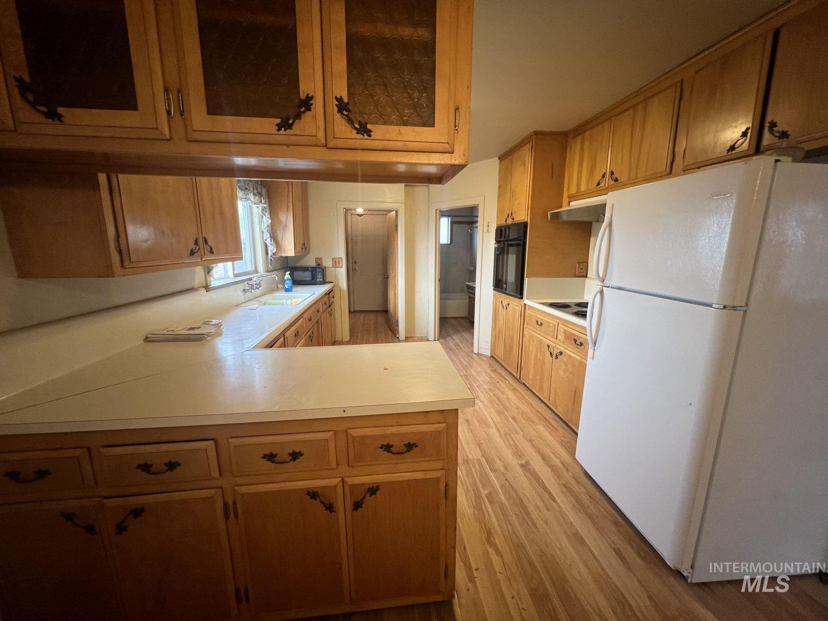 Kitchen featuring freestanding refrigerator, glass insert cabinets, light countertops, and light wood-type flooring