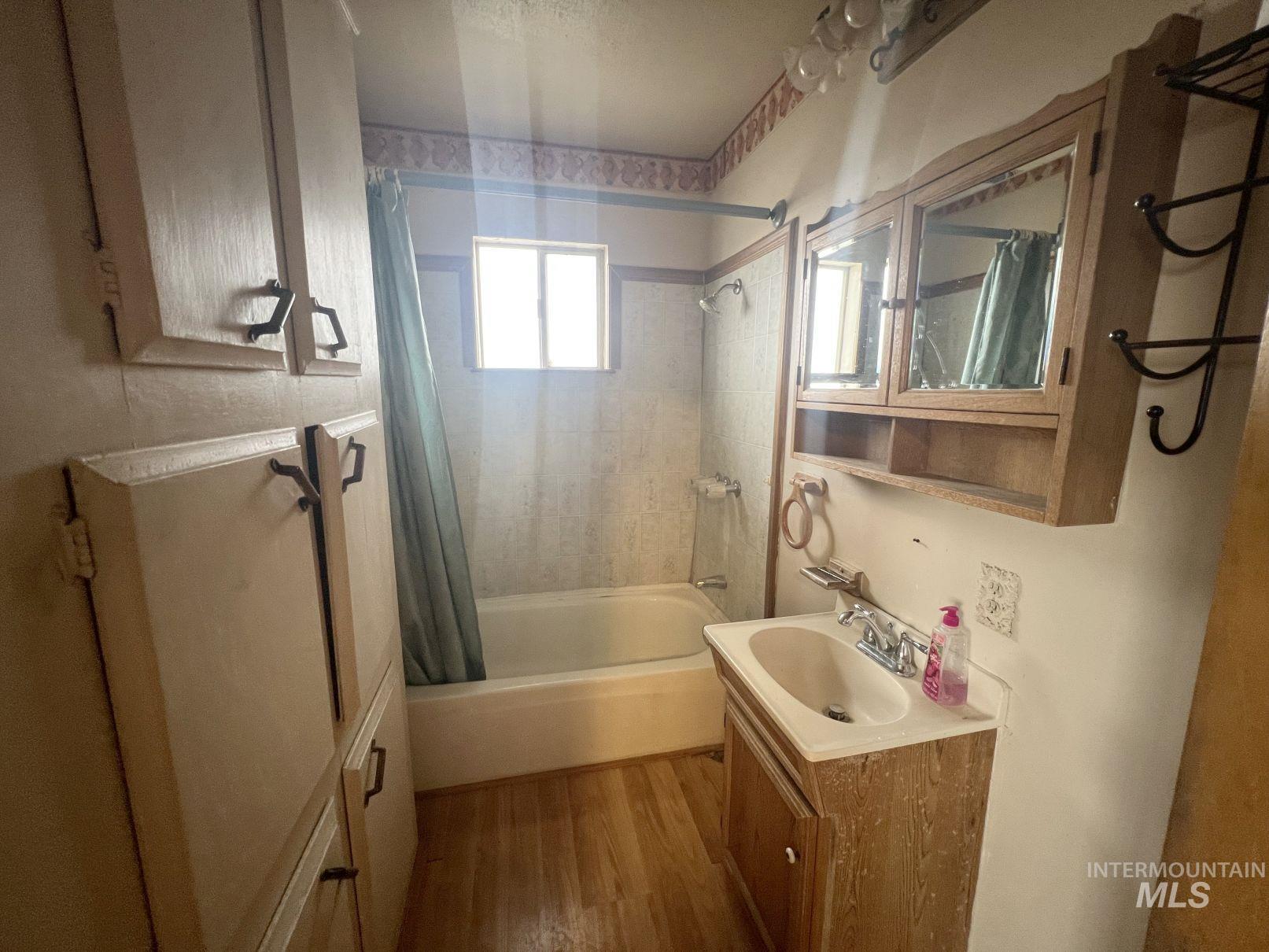 Bathroom featuring shower / bathtub combination with curtain, vanity, and dark wood-style flooring